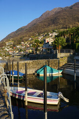 view of the marina with mirror reflection and colorful houses on the hill by lake Maggiore, Ticino