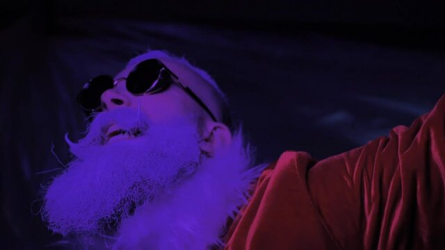 Energetic crazy excited Santa Claus dances, haves fun in vibrant neon lights at modern club party closeup indoor. Happy active celebration of New Year, Christmas, trendy style of holiday entertainment