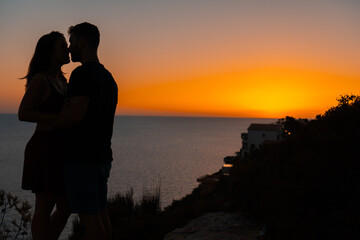 Young couple kiss each other at sunset from a cliff overlooking the sea