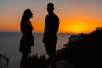 Young couple watching the sunset from a cliff overlooking the sea