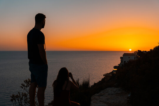 Young couple watching the sunset to take a picture from a cliff overlooking the sea