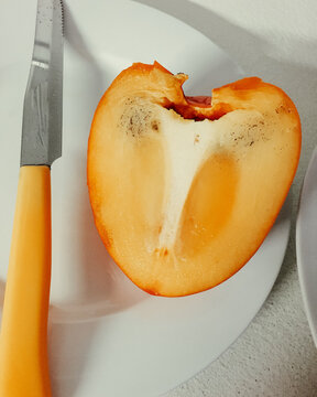 Slice of persimmon on white plate and yellow knife