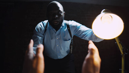Aggressive african policeman questioning the criminal using light techniques