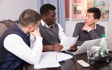 Three seriouse men are working with project and talking about documents together at home.