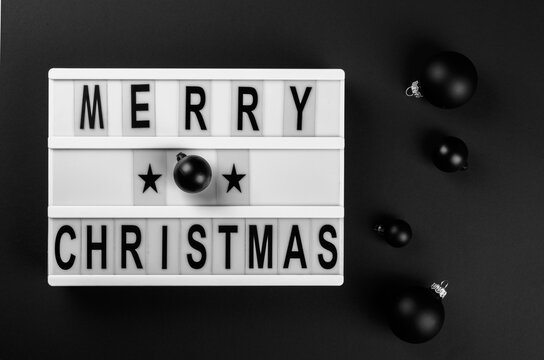 Lightbox with text message Merry Christmas. Traditional black decorative balls on a dark background .Creative Concept for Greeting Holiday Card. Flat lay top view