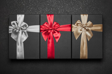Three gift boxes with a red gray and gold ribbon and large bows on dark granite..
