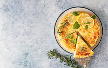 Lemon vanilla cheesecake decorated with rosemary, mint and lemon slices. Ricotta no crust cheesecake or casserole. Blue concrete background. Top view.