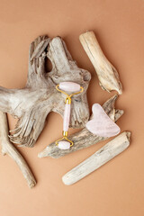 Jade face rollers and stone for beauty facial massage therapy. Flat lay on beige background with woody plant root - modern, trendy creative still life card, stylish luxury wellness concept