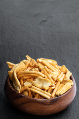 Savoury indian snack in wooden bowl on black stone background