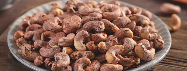 Cashew nuts with peel in a plate on wooden tray.