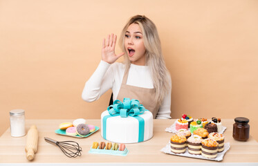 Teenager pastry chef with a big cake in a table shouting with mouth wide open