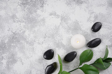 Black spa stones, candle, green plant on gray concrete background. Wellness concept. Top view, flat lay, copy space