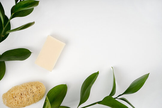 Soap, loofah sponge, green plant branches, white background. Hygiene, disinfection, natural product concept. Top view, flat lay, copy space