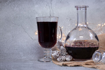 
A beautiful photo for a New Year's card or banner with warm mulled wine in a glass cup and a decanter on a gray background with burlap. Copy Space.