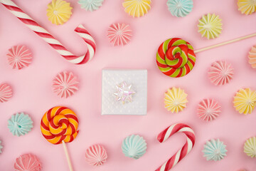 Present, colorful meringue, candy canes, lollipop on pink background. Sweets, Birthday, party concept, invitation. Top view, flat lay, copy space