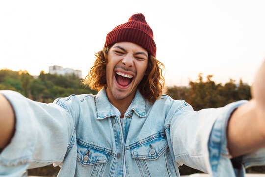 Cheerful young curly man taking a selfie by camera
