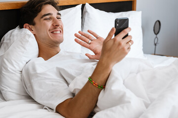 Positive man lies in bed and using mobile phone
