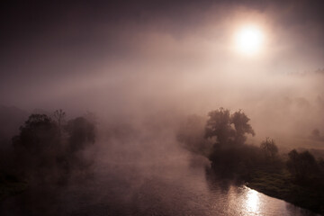 crazy foggy morning with hidden sun, autumn fog over the river with trees around