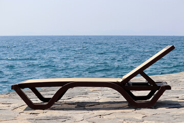 Empty deck chair on a stone beach on sea background. Beach vacation, quarantine during covid-19 coronavirus pandemic