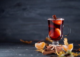 Glass of mulled wine with tangerines, cinnamon and anise on the table with dry autumn maple leaves,...