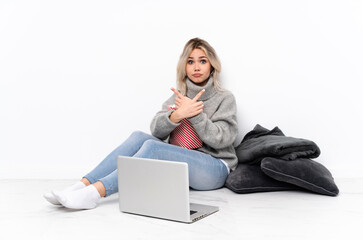 Teenager blonde girl eating popcorn while watching a movie on the laptop pointing to the laterals having doubts