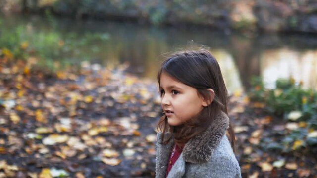 Little girl looking at a blurry black dog playing near a river in the forest