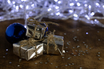A Christmas gift in silver paper and a Christmas tree toy - a blue ball on a background of white lights.