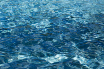 Light and dark blue water in a pool with slightly moving waves and reflections of the sun