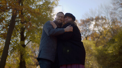Positive couple embracing nad smiling in city fall park