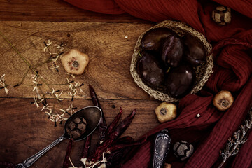Autumn still life . Fresh plums, red fabric and dried herbs on wooden background. 