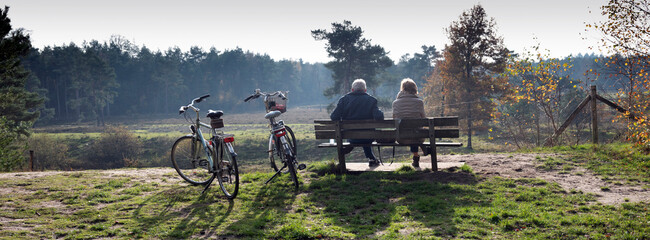 couple on bench resting from bicycle trip in autumn forest near Zeist in holland