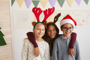 Portrait of three kids wearing Santa hats and looking at camera while enjoying class on Christmas, copy space