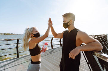 Young couple in protective masks  doing sports exercises at the beach pier. Athlete man and sportive woman jogging together on the quay near the sea.Sport, Active life. Covid-19.