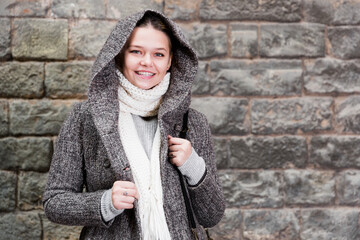 cheerful female in the historical city in coat hood near wall