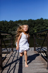 A six year old girl is wearing a white dress. Beautiful long hair. Walk near the river on the background of the forest