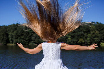 Naklejka premium A six year old girl is wearing a white dress. Beautiful long hair. Walk near the river on the background of the forest
