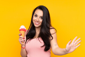 Young Colombian girl holding an cornet ice cream over isolated yellow background saluting with hand with happy expression