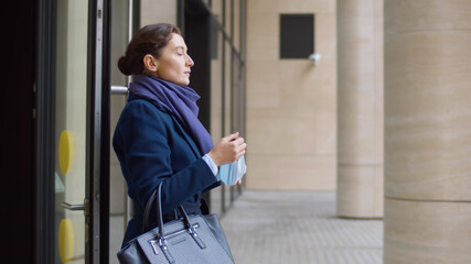 Business lady leaving office building and removing safety mask outdoors