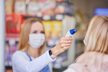 Adult woman in medical mask being checked for temperature in grocery store