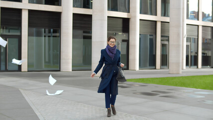 Excited businesswoman walking out business center throwing document away