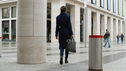 Back view of confident businesswoman wearing coat carrying briefcase walking outside