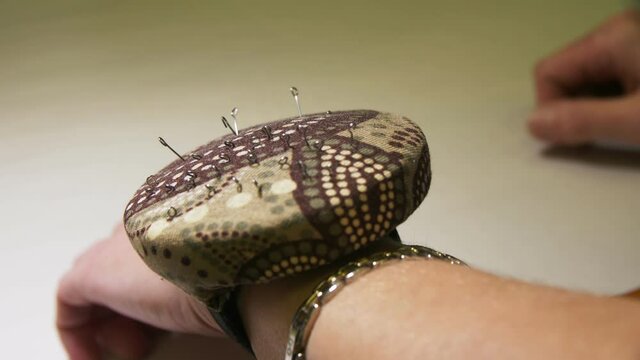 Seamstress puts metal pin into soft cushion on wrist closeup