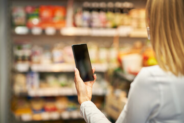 Adult woman in medical mask using smartphone and shopping for groceries