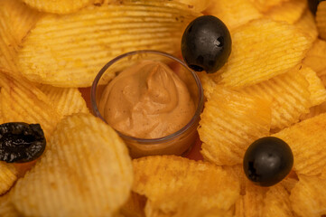 Crispy, delicious potato chips with mustard sauce and olives. Close up.