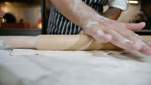 Close-up Hands of Bakery Cook Using Wooden Rolling Pin on Dough. Chef in Professional Kitchen Prepares Pastry with Flour to make Bread. Baker Rolling Cookie. Conception Healthy Eat at Home Cuisine 4k