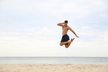 Fototapeta na wymiar Muscular man jumping on beach, space for text. Body training