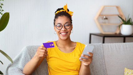 Black lady holding smartphone and credit card at home