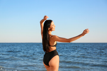 Beautiful young woman in black stylish swimsuit on beach