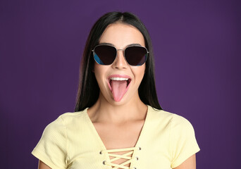 Beautiful woman wearing sunglasses on purple background