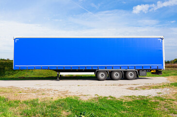 Brand new blue truck trailer waiting  by the road in a field, on  a bright summer day 